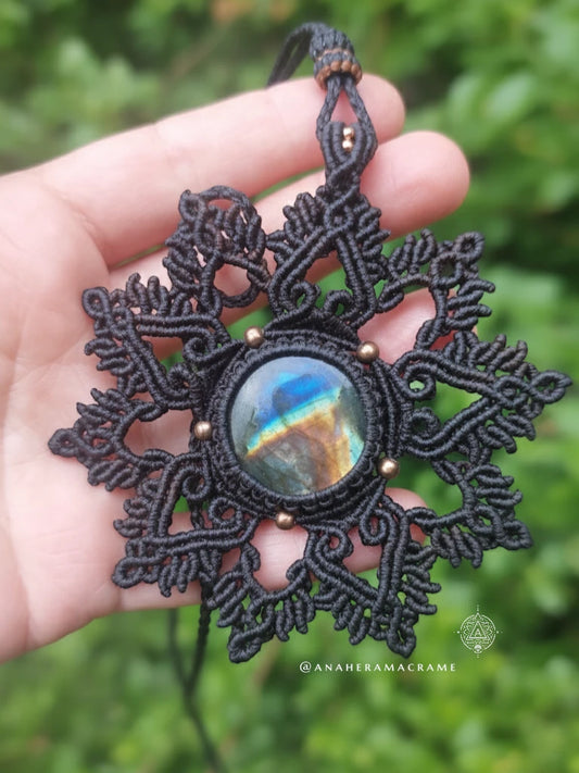 Brown lace pendant with a colorful stone held in a hand against a green leafy background