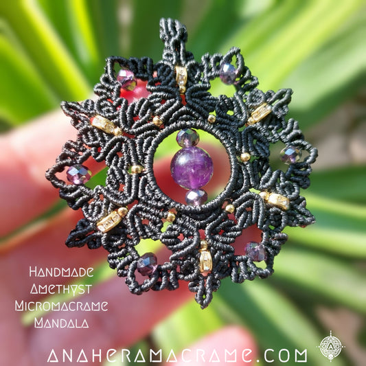 A black macrame mandala pendant necklace with purple rhinestone and gold-colored accents, displayed against a floral background.