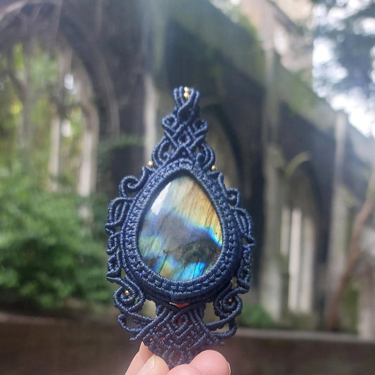 Close-up of a 60ct labradorite gemstone pendant wrapped in intricate blue macramé threadwork, glowing in natural light.