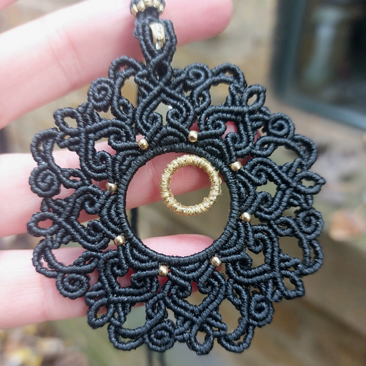 Black macrame mandala necklace featuring gold accents and a rondelle bead centerpiece, ideal for elegant and boho-inspired looks.
