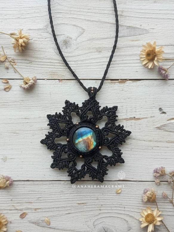 Brown lace pendant with a colorful center on a white wooden surface with dried flowers.
