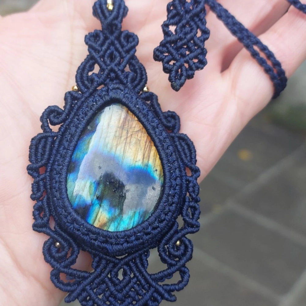 A blue macramé-wrapped pendant showcasing a flashy labradorite gemstone, shimmering under direct sunlight.