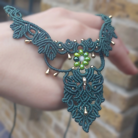 Green macrame choker with intricate floral design and gold accents.
