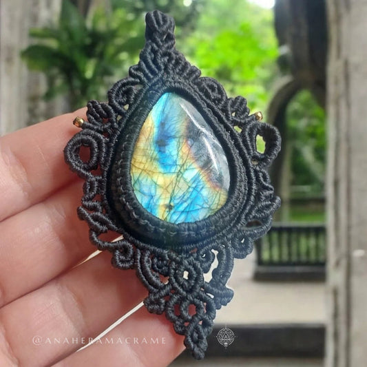 Labradorite necklace with shimmering blue and gold hues, held up against stone archway and greenery in background