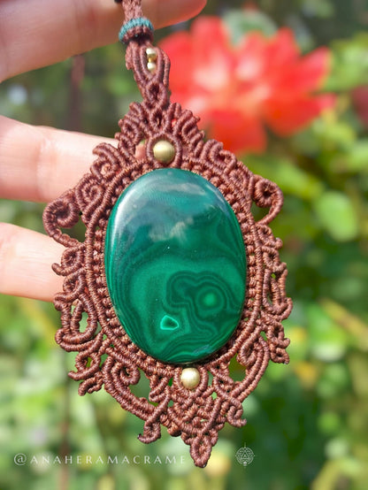 Close-up of green malachite pendant wrapped in intricate brown macrame with brass bead accents.