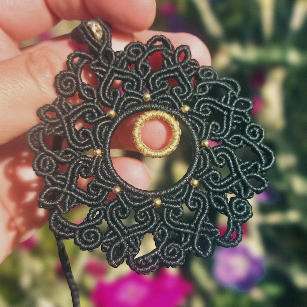 Elegant macrame mandala necklace with intricate black knotting and golden details, including a striking rondelle bead.
